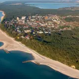 Widok z lotu ptaka na Jarosławiec, nadmorską miejscowość z piaszczystą plażą, lasami i zabudowaniami.