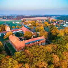 Zamek Bierzgłowski otoczony jesiennym lasem, z czerwonymi dachami i ceglanymi murami, w blasku zachodzącego słońca.