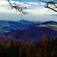 Widok na górzyste pasmo z drzewami w jesiennych barwach. Na szczycie jednego ze wzgórz widać budynki i zbiornik wodny. W oddali majaczy maszt telekomunikacyjny, przypominający czupel.