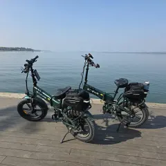 Dwa zielone rowery elektryczne z sakwami, gotowe na wyprawę z zasięgiem 200 km nad spokojną wodą.