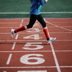 Biegacz na bieżni, skupiony na rytmie i kadencji w bieganiu, mija kolejne numery torów.