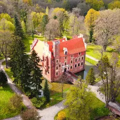 Zamek na wodzie w Wojnowicach, otoczony zielenią i drzewami, prezentuje się malowniczo.