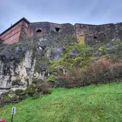 Potężny belfort wznosi się na skalistym zboczu porośniętym mchem. Kamienne mury i zielona trawa tworzą imponujący widok.