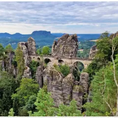 Kamienny most Bastei w Saksońskiej Szwajcarii, łączący skalne baszty pośród zielonych lasów i gór.