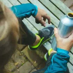 Osoba w sportowej kurtce i butach z neonowymi wstawkami trzyma metalową butelkę. W środku pewnie jest izotonik, idealny po wysiłku.