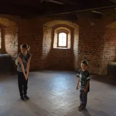Dzieci w komnacie z cegły w zamku w Bytowie, obok zabytkowych skrzyń.