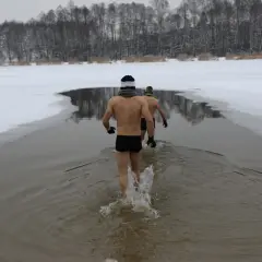 Dwóch mężczyzn w kąpielówkach wchodzi do lodowatej wody. Wokół śnieg i lód, zimowy krajobraz. To prawdziwy szok termiczny.