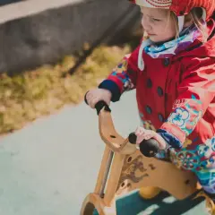 Mała dziewczynka w czerwonej kurtce na rowerku biegowym. Od jakiego wieku można zacząć przygodę z takim pojazdem?