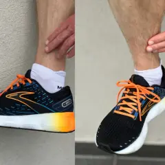 Biegacz pokazuje ból w łydce, który może być objawem shin splints. Na nogach ma czarne buty sportowe Brooks z pomarańczowymi sznurówkami.