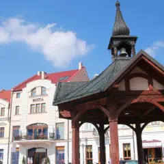 Rzeszów rynek z drewnianą altaną i kamienicami. Słońce świeci, a na niebie widać chmury.