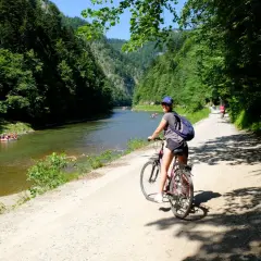 Dziewczyna na rowerze na malowniczej trasie rowerowej w Szczawnicy. W oddali widać tratwy na rzece.