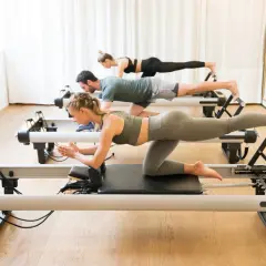 Trzy osoby ćwiczą na reformerach. To świetny sposób, by dowiedzieć się, pilates co to jest i jak poprawić sylwetkę.