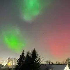 Zielona i czerwona zorza polarna nad domami. Zastanawiasz się, ile trwa zorza polarna? To zjawisko może trwać od kilku minut do kilku godzin.