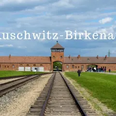 Brama obozowa Auschwitz-Birkenau, gdzie historia przypomina o tragedii. Tłum zwiedzających podąża torami.