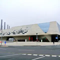 Futurystyczny budynek w Wolfsburg miasto, z betonowymi elementami i przeszklonymi fragmentami.