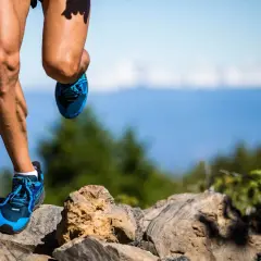 Nogi biegacza w niebieskich butach na kamienistym szlaku, przygotowującego się do ultramaratonu. Ile km jeszcze przed nim?