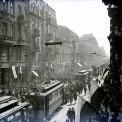 Tłum ludzi i tramwaje na ulicy Piotrkowska w Łodzi. Widać kamienice, flagi i napisy na sklepach.