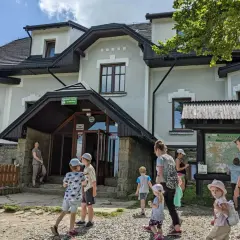 Rodzina zwiedza schronisko na Magurce Wilkowickiej. Dzieci z rodzicami przyglądają się mapie turystycznej.