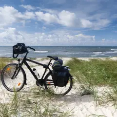 Rower z sakwami na piaszczystej plaży, gotowy na odkrywanie tras rowerowych nad morzem. Błękitne niebo i fale tworzą idealne tło.