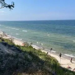 Piękny widok na plażę i morze. Ludzie spacerują brzegiem, a w oddali widać drzewa. Miejsce idealne na orzechowo-słodkie lenistwo.
