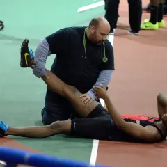 Fizjoterapeuta pomaga biegaczowi po ćwiczeniach, rozciągając jego nogi. Może to być część treningu wzmacniającego mięśnie dwugłowe uda, podobnego do nordic curls.