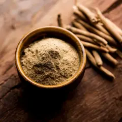 Proszek z ashwagandhy w miseczce i korzenie obok. Kiedy brać ashwagandhę? Najlepiej rano lub wieczorem.