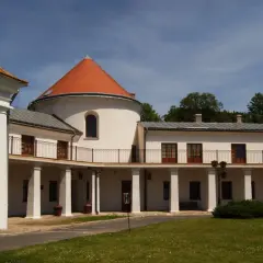 Zamek w Lesku z okrągłą wieżą i arkadowym gankiem, otoczony zielenią.