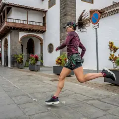 Kobieta w sportowym stroju biegnie po brukowanej ulicy przed białym budynkiem.