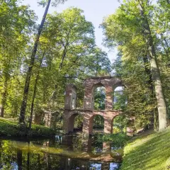 Ruiny akweduktu w Arkadii Nieborów, otoczone bujną zielenią i odbijające się w spokojnej wodzie.