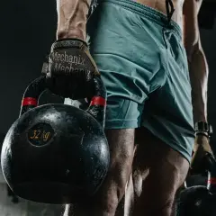 Mężczyzna w rękawicach Mechanix trzyma ciężkie kettlebelle, przygotowując się do wyzwania HYROX.