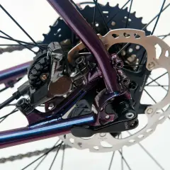 Błyszcząca, fioletowa rama roweru z widoczną sztywną osią, przerzutką Shimano i tarczą hamulcową.