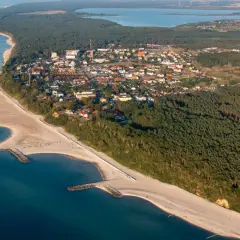 Widok z lotu ptaka na Jarosławiec, nadmorską miejscowość z piaszczystą plażą, lasami i zabudowaniami.