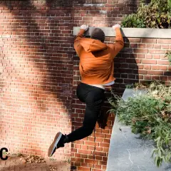 Młody człowiek wspina się po ceglanej ścianie, pokazując, czym jest parkour.