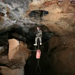 Odważny speleolog wspinający się po linie w jaskini, z workiem na sprzęt zwisającym poniżej.