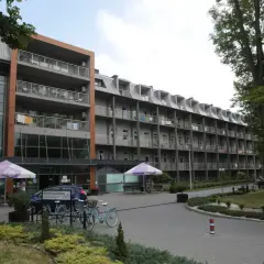 Budynek sanatorium z balkonami i drzewami. Miejsce idealne do wypoczynku i regeneracji, gdzie balneologia odgrywa kluczową rolę.