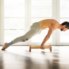 Mężczyzna wykonuje ćwiczenie planche na drewnianych poręczach, z nogami wyprostowanymi w powietrzu.