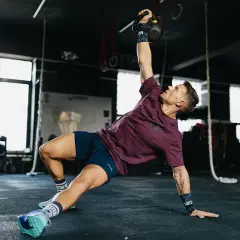Mężczyzna wykonuje ćwiczenia gimnastyczne z kettlebell, unosząc go nad głowę.