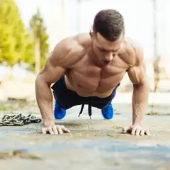 Mięśniowy mężczyzna wykonuje pompki na biceps na zewnątrz. Obok leży ciężki łańcuch, symbolizujący trudny trening.