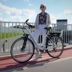 Kobieta z rowerem elektrycznym na moście. Czy na rower elektryczny trzeba mieć prawo jazdy? Zależy od jego mocy.
