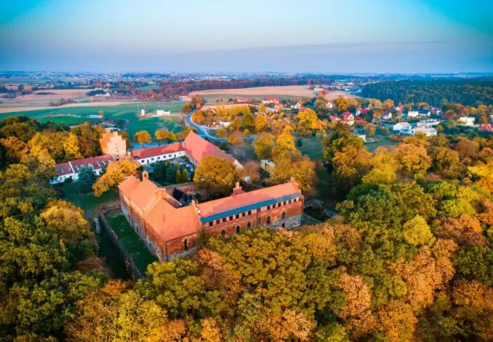 Zamek Bierzgłowski otoczony jesiennym lasem, z czerwonymi dachami i ceglanymi murami, w blasku zachodzącego słońca.