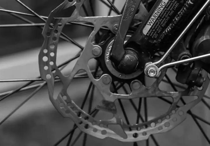 Tarcza hamulcowa i szprychy roweru. Widoczny mechanizm przerzutek Shimano i ostrzeżenie.