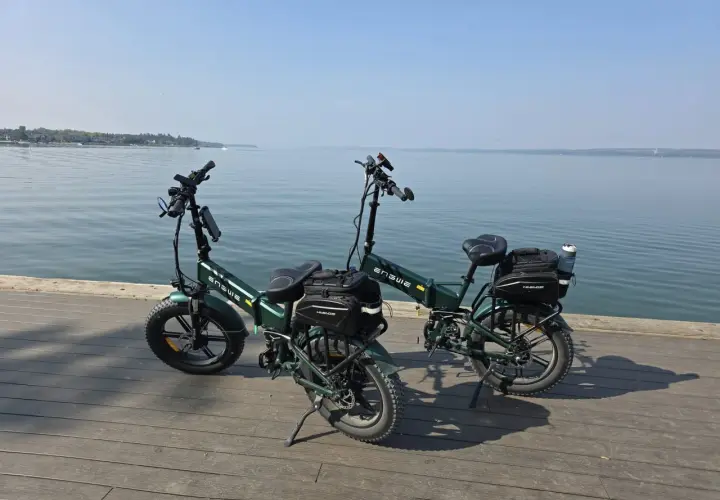 Dwa zielone rowery elektryczne z sakwami, gotowe na wyprawę z zasięgiem 200 km nad spokojną wodą.
