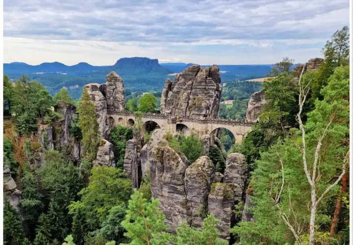 Kamienny most Bastei w Saksońskiej Szwajcarii, łączący skalne baszty pośród zielonych lasów i gór.