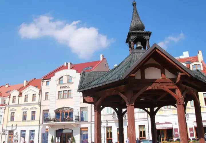 Rzeszów rynek z drewnianą altaną i kamienicami. Słońce świeci, a na niebie widać chmury.