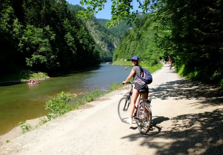 Dziewczyna na rowerze na malowniczej trasie rowerowej w Szczawnicy. W oddali widać tratwy na rzece.