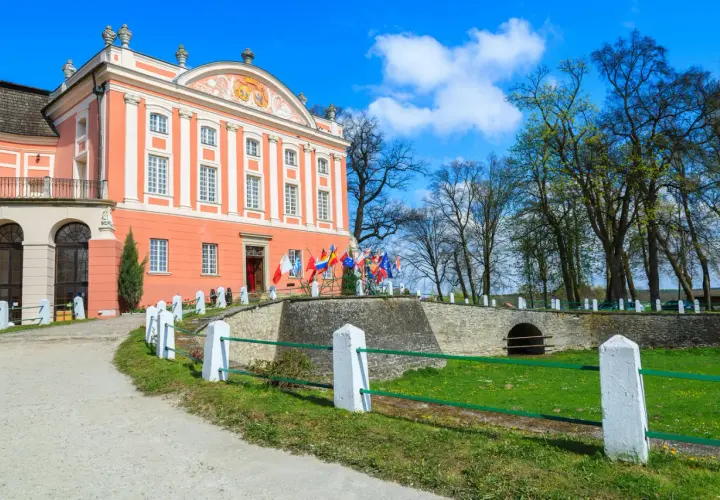 Pałac w Kurozwękach, z licznymi flagami przed wejściem, zaprasza do odkrywania jego atrakcji.