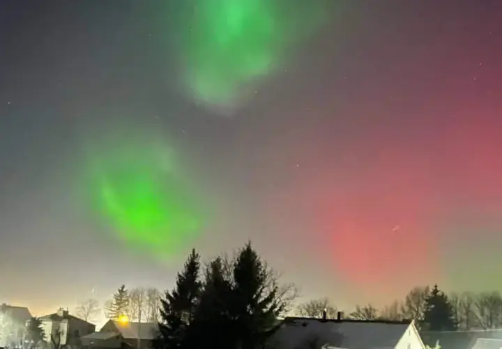 Zielona i czerwona zorza polarna nad domami. Zastanawiasz się, ile trwa zorza polarna? To zjawisko może trwać od kilku minut do kilku godzin.