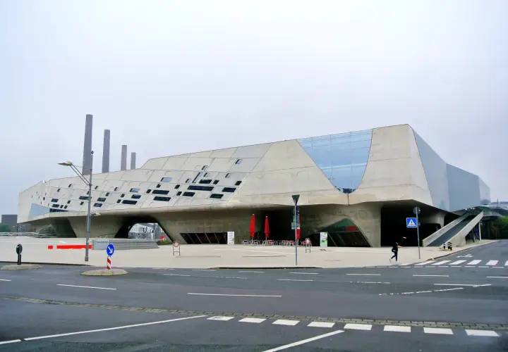Futurystyczny budynek w Wolfsburg miasto, z betonowymi elementami i przeszklonymi fragmentami.