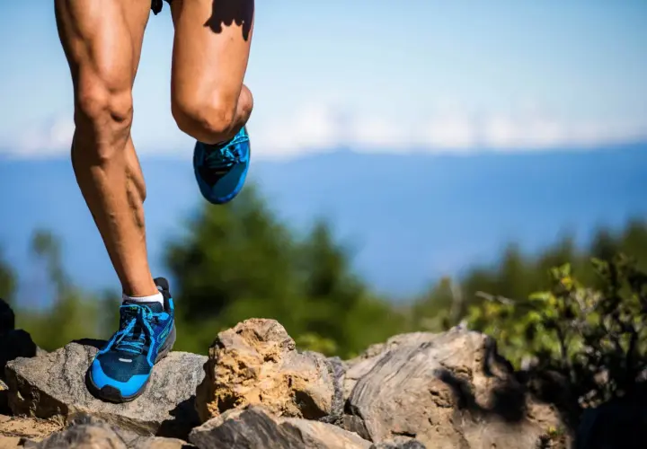 Nogi biegacza w niebieskich butach na kamienistym szlaku, przygotowującego się do ultramaratonu. Ile km jeszcze przed nim?