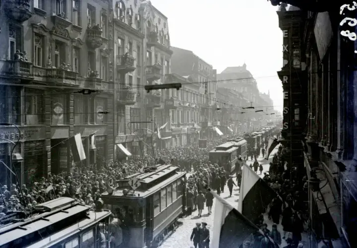 Tłum ludzi i tramwaje na ulicy Piotrkowska w Łodzi. Widać kamienice, flagi i napisy na sklepach.